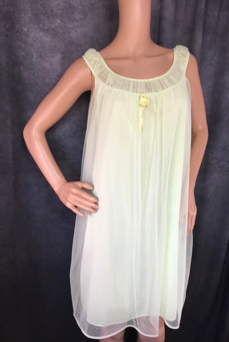 May include: A pale yellow, sheer, sleeveless nightgown with a ruffled neckline and a satin bow at the center.
