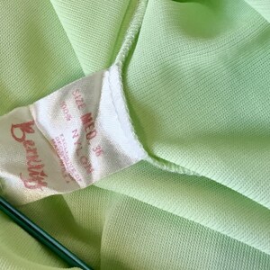 May include: A white tag with the text "Beauty" in red lettering and "Size Med 36 100% Nylon" in black lettering. The tag is attached to a light green fabric.