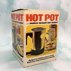 May include: A white box with a red and black 'HOT POT' logo. The box features a silver electric kettle with a black handle and a black base. The text on the box reads '...makes instant hot water!' and 'Perfect for instant soup or broth. Boils four cups of water in 5 minutes.'