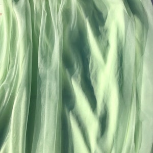 May include: A light green sheer fabric with a soft, flowing texture. The fabric is draped and folded, creating a delicate and airy appearance.