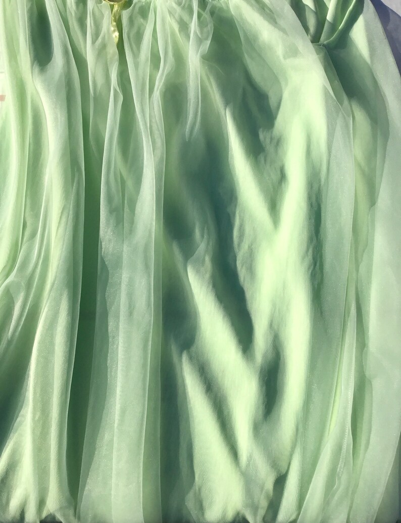 May include: A light green sheer fabric with a soft, flowing texture. The fabric is draped and folded, creating a delicate and airy appearance.