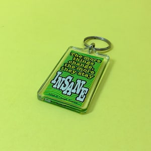 May include: Green and white keychain with the text "The more things change, the more they stay INSANE" and the copyright information "1056 © Laugh Tracks".