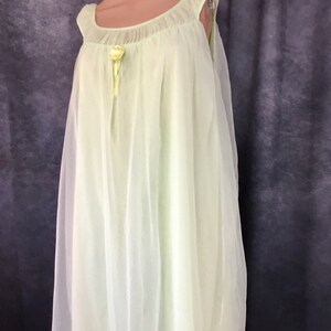 May include: A pale green, sheer, sleeveless nightgown with a gathered neckline and a small yellow flower accent at the center.