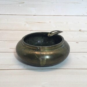 May include: A vintage brass ashtray with a hinged lid. The ashtray is round and has a dark brown patina.