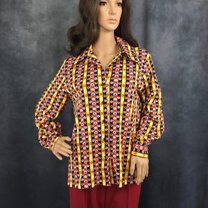 May include: A long-sleeved button-up shirt with a colorful geometric pattern in shades of yellow, red, white, and black. The shirt has a pointed collar and a button-up front.