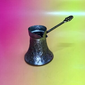 May include: A silver Turkish coffee pot with an ornate floral design. The pot has a long handle with a decorative end.