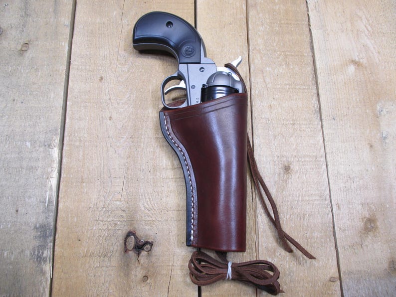 May include: A brown leather holster with a silver revolver inside. The holster has a strap and a loop for attaching to a belt.