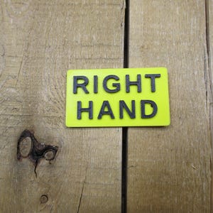 May include: A rectangular, neon yellow sign with the words "RIGHT HAND" in bold, black capital letters. The sign is set against a backdrop of weathered, light brown wooden planks.