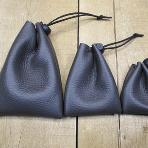 May include: Three brown leather drawstring pouches of varying sizes. The pouches are made of a textured leather and have black drawstrings.