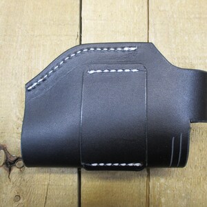May include: Black leather holster with white stitching. The holster has a curved top, a belt loop, and a small strap with a snap closure. The item is designed to hold a small object.
