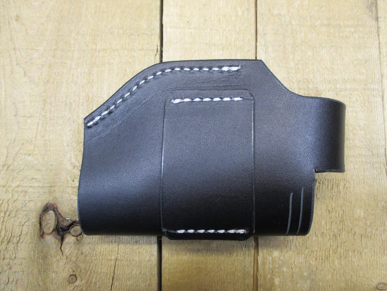 May include: Black leather holster with white stitching. The holster has a curved top, a belt loop, and a small strap with a snap closure. The item is designed to hold a small object.