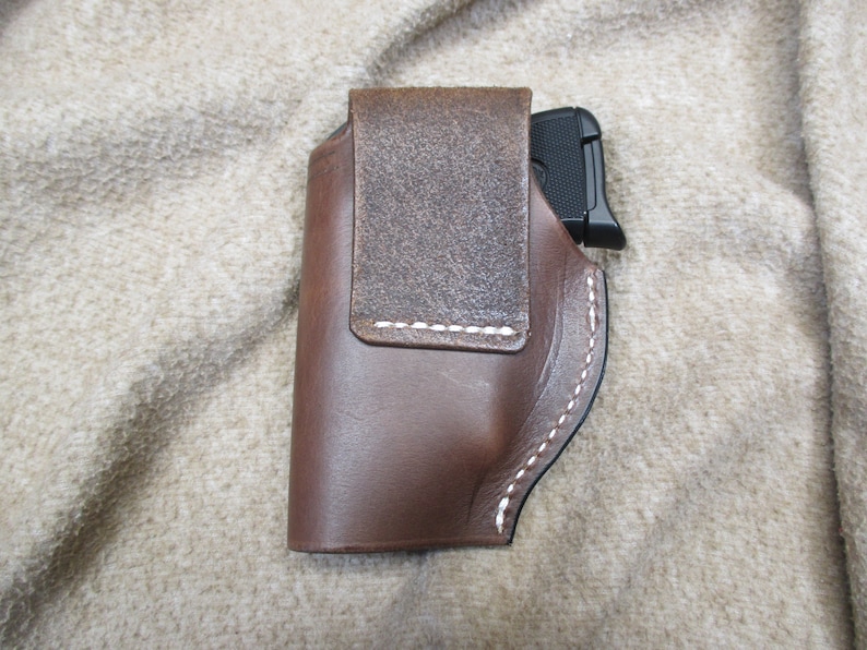 Może przedstawiać: Brązowa sk&oacute;rzana kabura z białymi szwami do małego pistoletu.