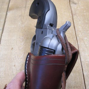 May include: A silver revolver is partially visible in a brown leather holster. The holster has white stitching and a leather strap. The revolver has a black grip and a silver barrel.