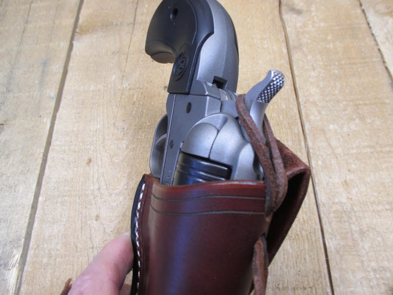 May include: A silver revolver is partially visible in a brown leather holster. The holster has white stitching and a leather strap. The revolver has a black grip and a silver barrel.