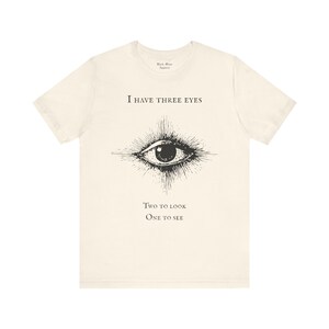 May include: A white t-shirt with a black eye graphic and the text "I have three eyes. Two to look. One to see."