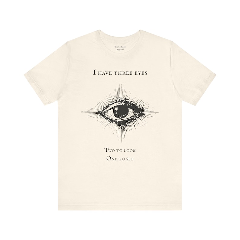 May include: A white t-shirt with a black eye graphic and the text "I have three eyes. Two to look. One to see."