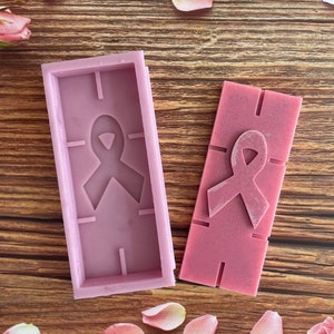 Op de afbeelding: Twee roze siliconen mallen voor het maken van kaarsen of zeep. De mallen zijn rechthoekig en hebben een reliëf roze lintontwerp.