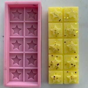 May include: A pink silicone mold with 12 star-shaped cavities and a yellow wax melt with 6 star-shaped sections, each with gold glitter.