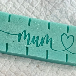 May include: A teal blue rectangular block with the word "Mum" written in cursive script and a heart symbol.