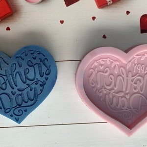 May include: Two heart-shaped silicone molds for making resin crafts. The molds are blue and pink and feature the text "Happy Mother's Day" in a decorative font.