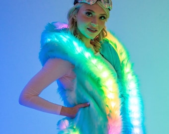May include: A turquoise faux fur vest with a rainbow LED light trim. The vest has a hood and is worn by a person with blonde hair wearing a pink and white ski mask.