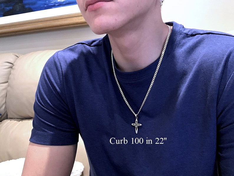 May include: A silver curb chain necklace with a silver cross pendant. The chain is 22 inches long and the text "Curb 100 in 22" is printed on a blue t-shirt.