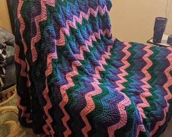 May include: A crocheted blanket with a chevron pattern in shades of pink, green, and blue. The blanket is draped over a chair.