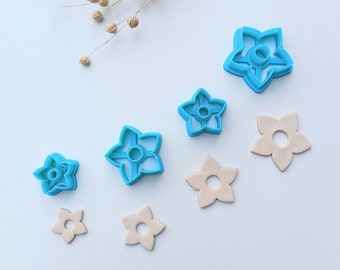 Peut inclure: Un ensemble de six emporte-pièces en plastique en forme de fleur, bleus et beiges. Les emporte-pièces sont disposés en rangée du plus grand au plus petit.