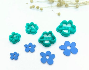 Peut inclure: Un ensemble de six emporte-pièces en forme de fleur turquoise et six découpes de fleurs en papier bleu. Les emporte-pièces sont de tailles différentes et ont un bord surélevé. Les découpes en papier sont toutes de la même taille et ont un design simple.
