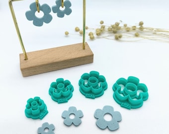 May include: Set of six turquoise flower-shaped cookie cutters, with sizes ranging from 1.125 inches to 1.5 inches in diameter. The cutters are displayed on a wooden stand with two light blue flower-shaped earrings.