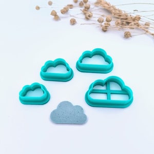 Może przedstawiać: Zestaw czterech ciasteczek w kształcie chmury w kolorze turkusowym, z których jeden ma wzór kratki wewnątrz. W zestawie znajduje się również ciasteczko w kształcie chmury w kolorze szarym.