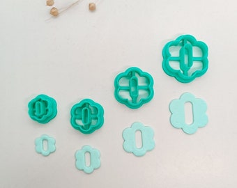 Könnte beinhalten: Eine Sammlung von türkis- und hellblauen Polymer Clay Ausstechern in verschiedenen Größen und Formen. Die Ausstecher haben die Form einer Blume mit einer zentralen Öffnung. Einige sind massiv, andere haben ein ausgeschnittenes Design. Die Ausstecher sind auf einer weißen Oberfläche angeordnet.