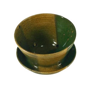 Può includere: Un vaso di ceramica verde e marrone con fori di drenaggio. Il vaso ha un sottovaso.