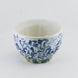 May include: A small white ceramic bowl with a blue and white floral pattern. The bowl is round and has a slightly flared rim.