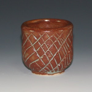 Può includere: Una piccola tazza in ceramica marrone con un motivo testurizzato a forma di diamante. La tazza ha una glassa blu chiaro all'interno.