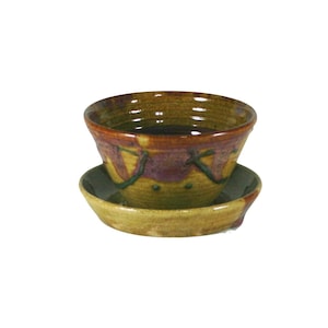 May include: A brown and green ceramic planter with a saucer. The planter has a unique design with brown, green, and purple accents.