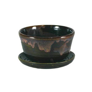 May include: A dark green ceramic planter with a pink and brown glaze. The planter has a saucer.
