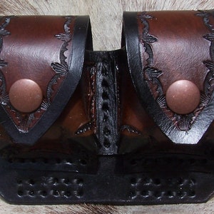 May include: A brown leather double pouch with black trim and copper snaps. The pouch has a decorative embossed design.