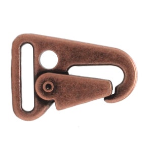 May include: A copper-toned metal trigger snap clasp with a D-ring. The clasp is designed for attaching straps, leashes, or other accessories.