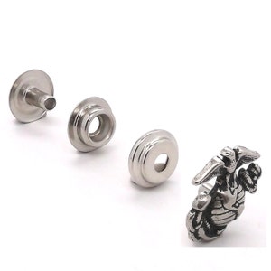 May include: A set of silver-toned metal snap fasteners with a decorative eagle emblem. The fasteners are designed for attaching fabric or leather.
