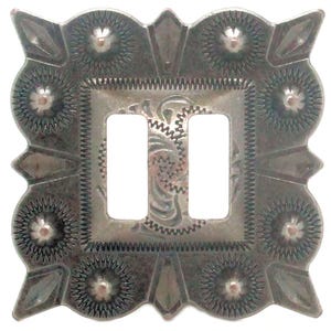 May include: A silver-toned, decorative light switch cover with a rectangular center featuring two openings. The cover has an ornate, embossed design with floral and geometric patterns, including sunburst and diamond shapes.