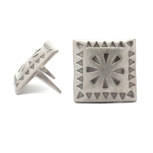 May include: Two silver metal decorative studs with a geometric design. The studs have a square shape with a raised center and a starburst pattern. The studs have a pointed base for attaching to a surface.