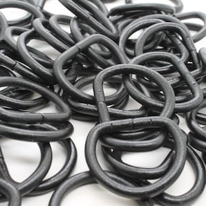 May include: A pile of black, D-shaped metal rings. The rings are tightly packed together, with a matte finish. The image is a close-up shot, highlighting the texture and shape of the rings. The rings appear to be made of a durable material.