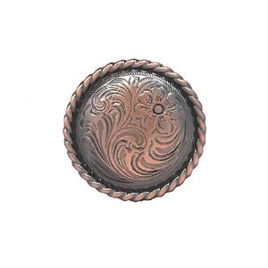 May include: A round, copper-colored metal button with an ornate floral design in the center. The button has a twisted rope-like border. The design is embossed and detailed, giving it a vintage or Western aesthetic.