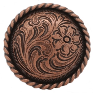 May include: A round copper-toned metal button featuring an intricate embossed floral and scrollwork pattern on its surface. The button is framed by a decorative twisted rope-style border, creating a textured edge around the central design.