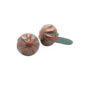 May include: Two copper-colored metal tacks with a turquoise green finish. The tacks have a round head with a decorative design and a short, straight shank.