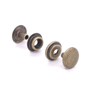 May include: Three antique brass snap fasteners, consisting of a stud, a cap, and a socket. The fasteners are used for attaching fabric or leather together.