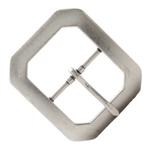 May include: Silver-toned metal buckle with a rectangular shape and a rounded, octagonal frame. The buckle has a single prong and a pin that slides through a hole in the strap.