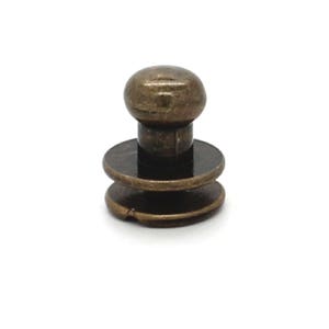 May include: A brass-colored snap fastener with a round head and a double-layered base.