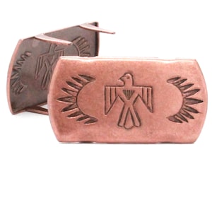 May include: Two copper-colored metal buckles with a stylized bird design. The bird is surrounded by a sunburst pattern.